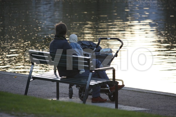 Young parent sitting on a bench with a baby in Helsinki, Finland.